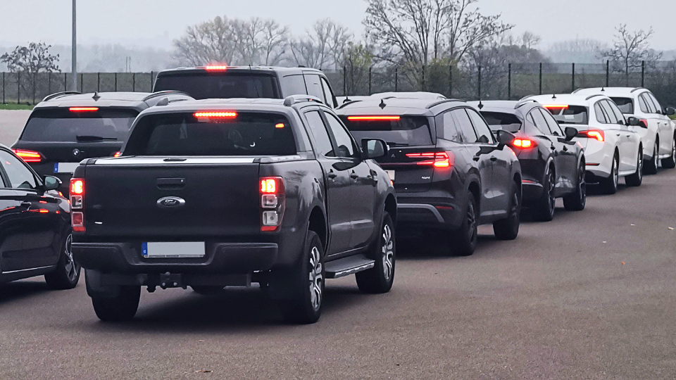 Autoschlange in einer Reihe an einem grauen Tag; Bremslichter leuchten, während ein grauer Ford-Pickup eine Firmen-Fahrsicherheitsveranstaltung anführt.